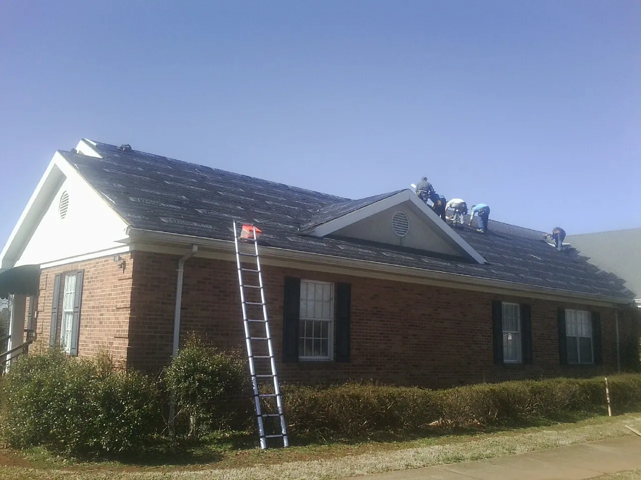 Crew tearing shingles off a brick ranch roof with a ladder set — Emergency Roof Repair work by our crew in Hershey