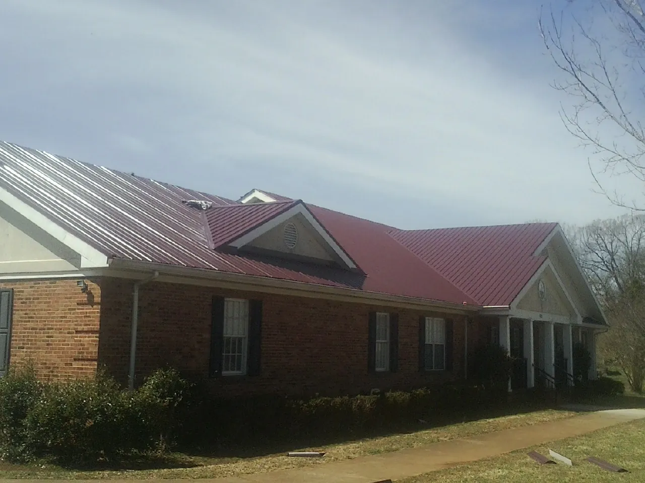 Red metal roof with gabled entries on a long brick building, from a Hail Damage Roof Repair job in Hershey