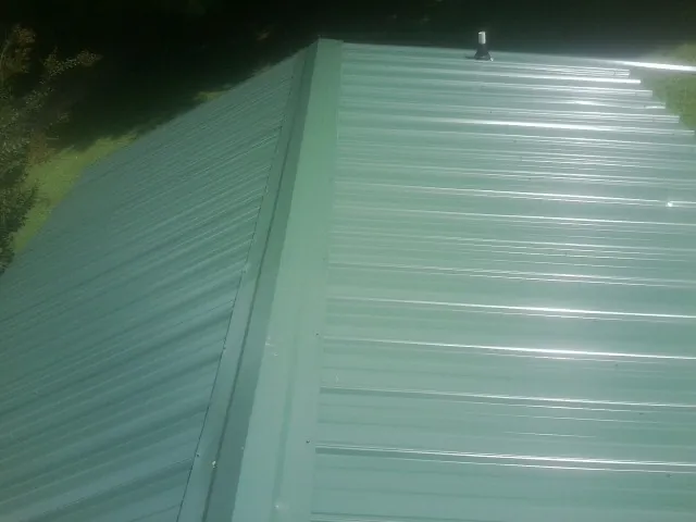 New green metal panels meeting at the ridge of a roof — Flat Roof Repair work by our crew in Hershey