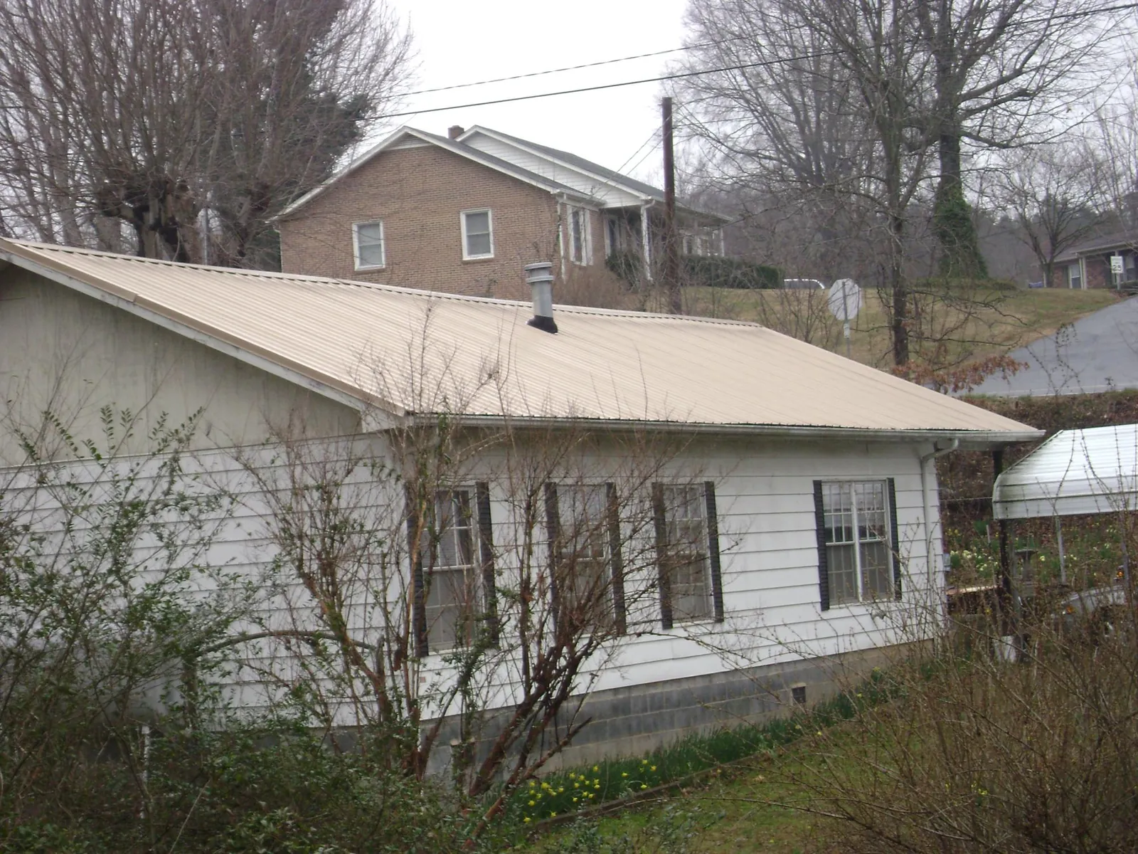 Tan metal roof on a white sided house set into a hillside — Commercial Roofing by Roofing Brothers in Hershey